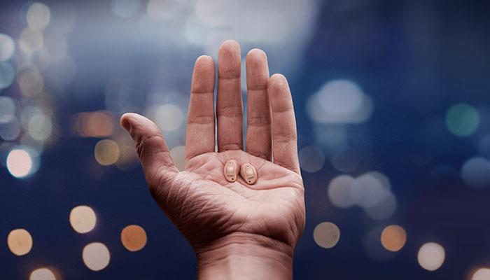 A hand holding practically invisible ReSound LiNX Quattro hearing aids