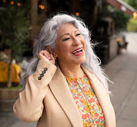 Lächelnde Frau drückt die Taste an ihrem Hörsystem